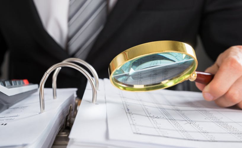 Businessman Examining Invoice With Magnifying Glass