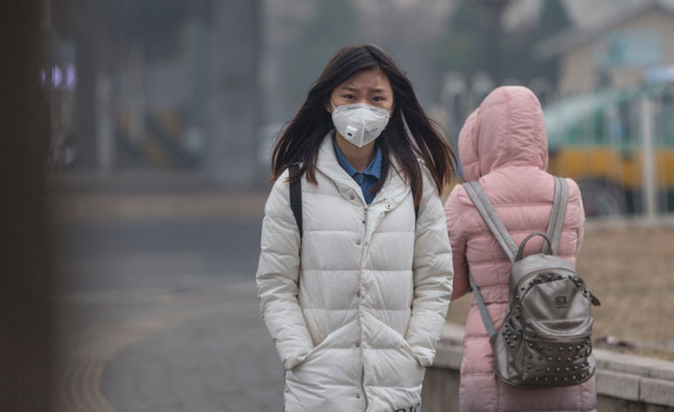 Beijing, China - December 7, 2015: Asian girl protects herself against air pollution by wearing mouth mask with air filter. A incidental people on the background.