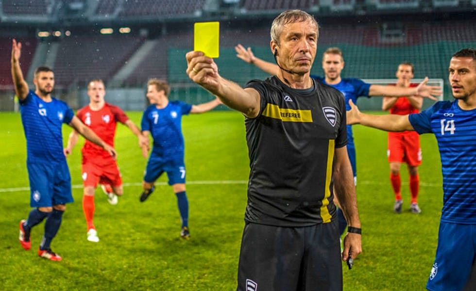 Soccer referee surrounded by players of both teams while he is holding a yellow card.