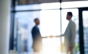 Blurred shot of two businessmen shaking hands in a modern office for feature on international law firms in Ireland