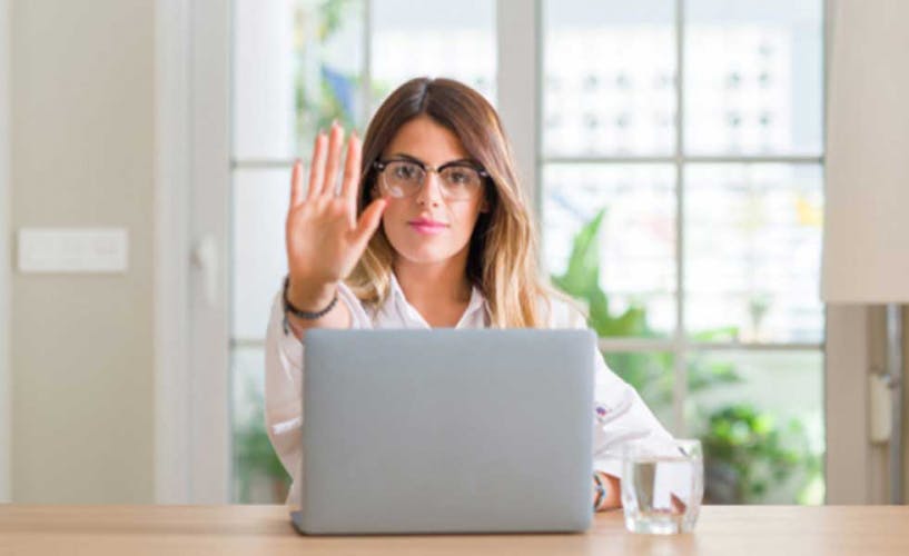 Young woman at home using laptop with open hand doing stop sign with serious and confident expression, defense gesture